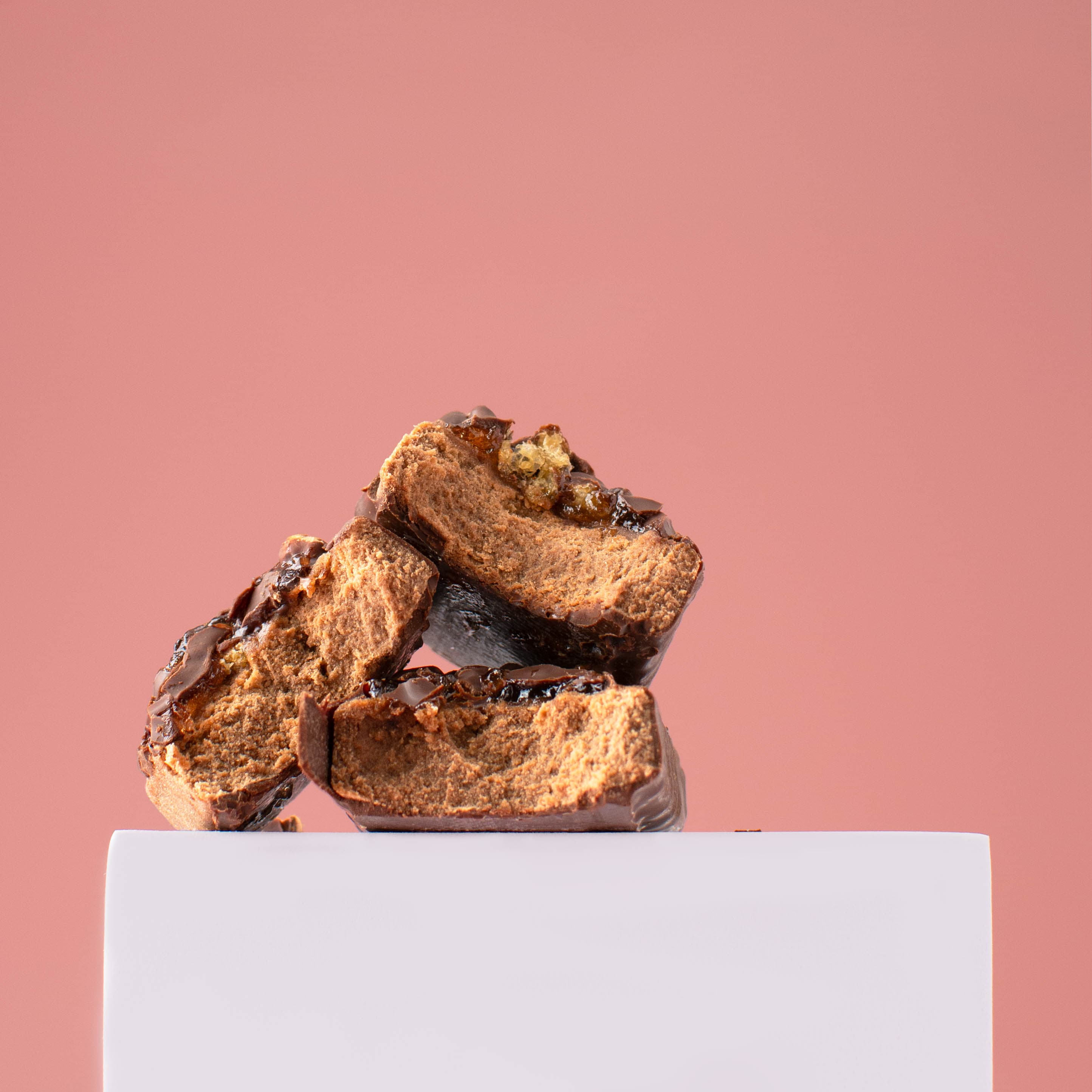 Stacked chocolate flapjack pieces on a plinth against coral pink