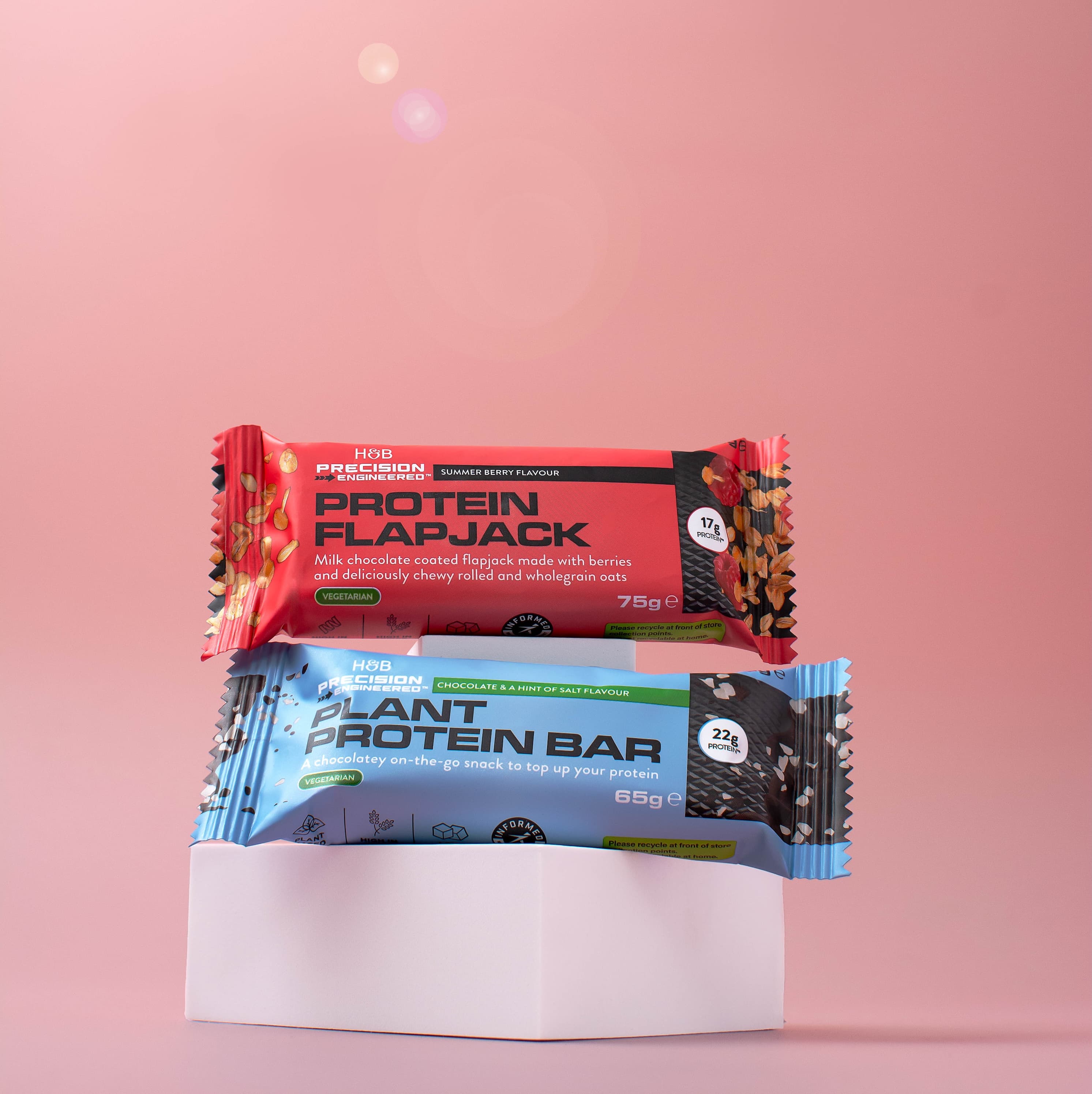 Protein snack bars stacked on a plinth against a pink background