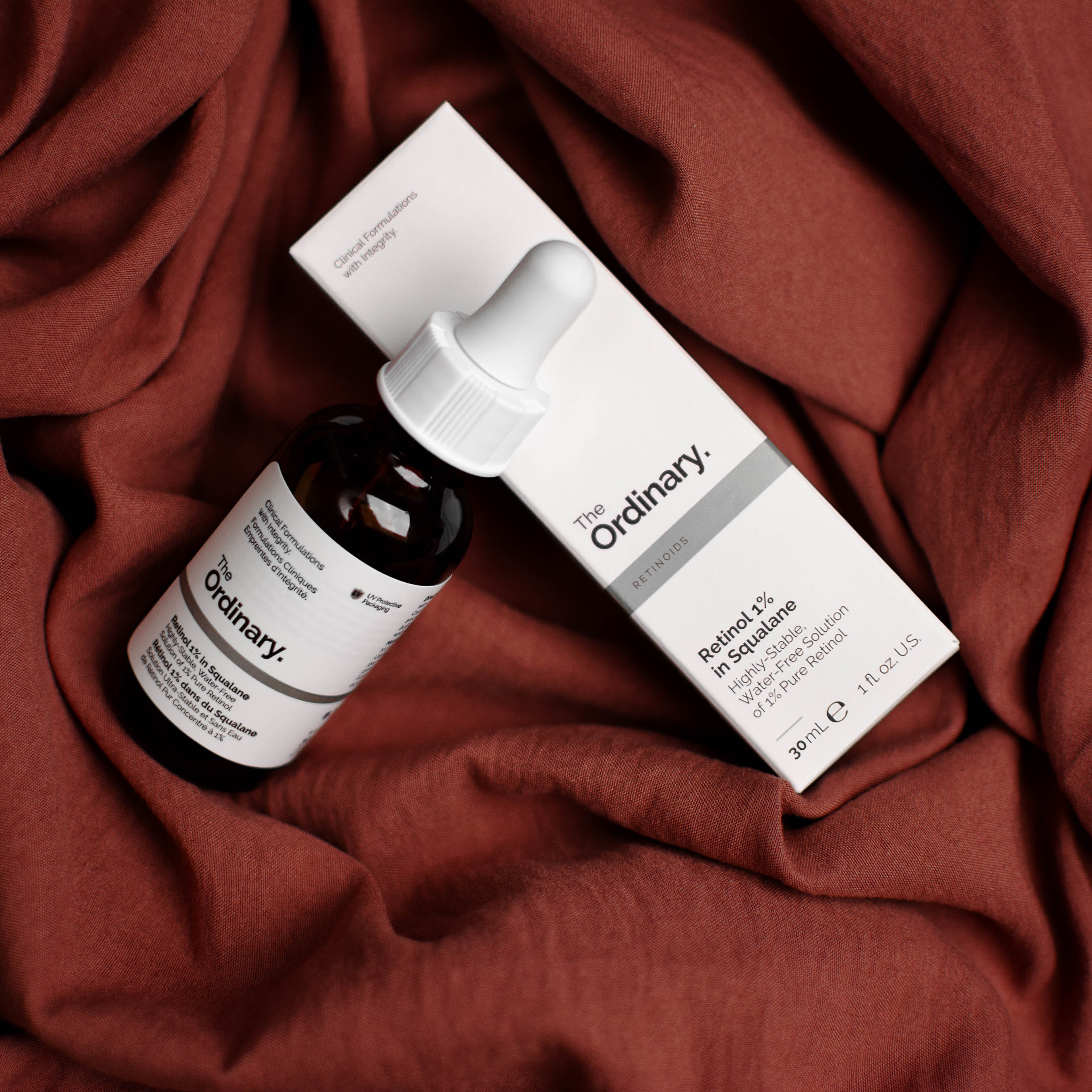 The Ordinary skincare bottle and carton styled on burgundy fabric