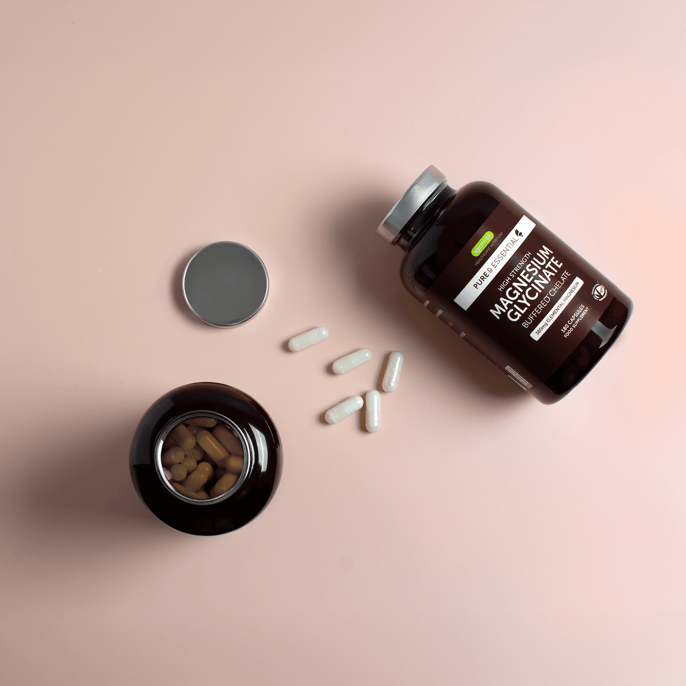 Magnesium supplement bottle, lid and capsules in a pink flat lay