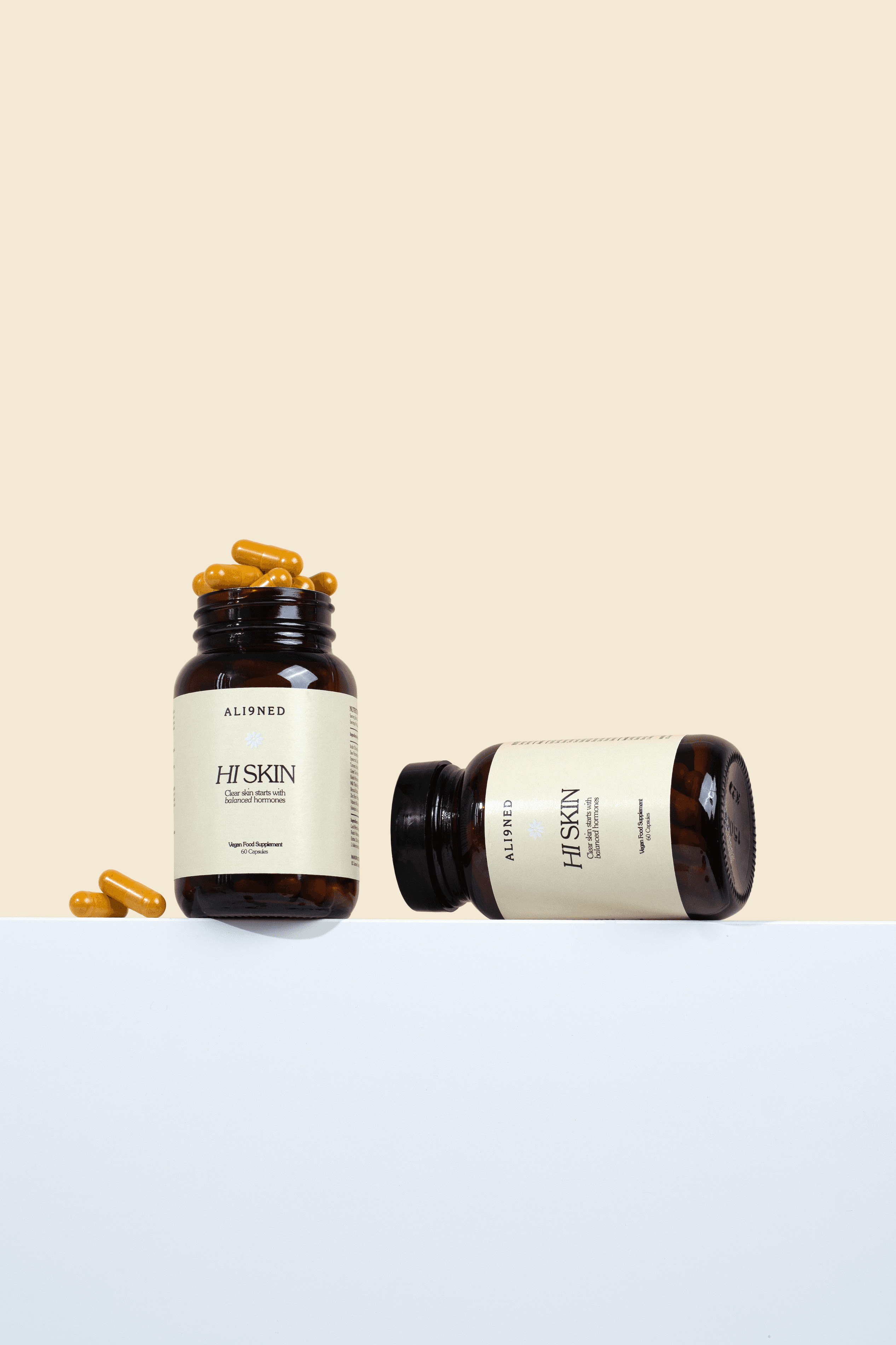 Two supplement bottles with golden capsules on a pale plinth